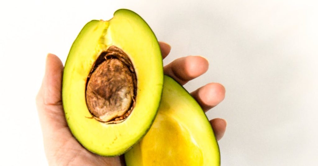 A hand holding ripe avocado halves with seed on white background. Perfect for healthy eating themes.