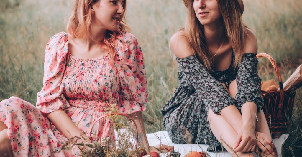 Two women sit on a blanket having a picnic outdoors, enjoying a sunny day.