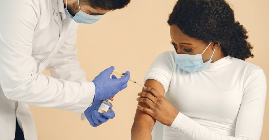 A healthcare professional giving a vaccination to a seated woman, both wearing masks.