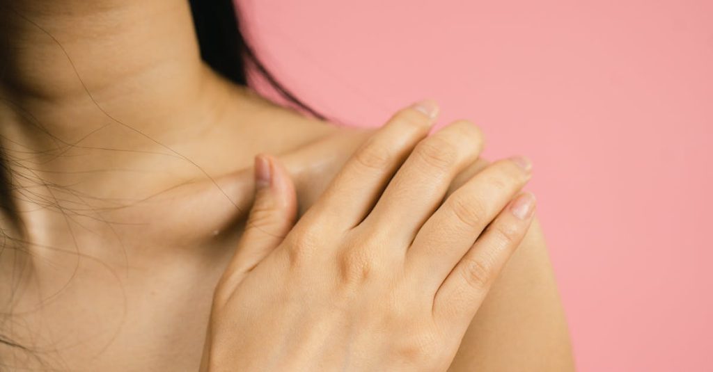 Close-up of a woman's hand resting on her shoulder against a pink backdrop, highlighting skin and nails.