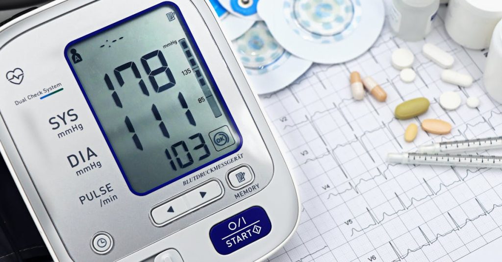 Close-up of a digital blood pressure monitor with ECG printout, pills, and medical tools.