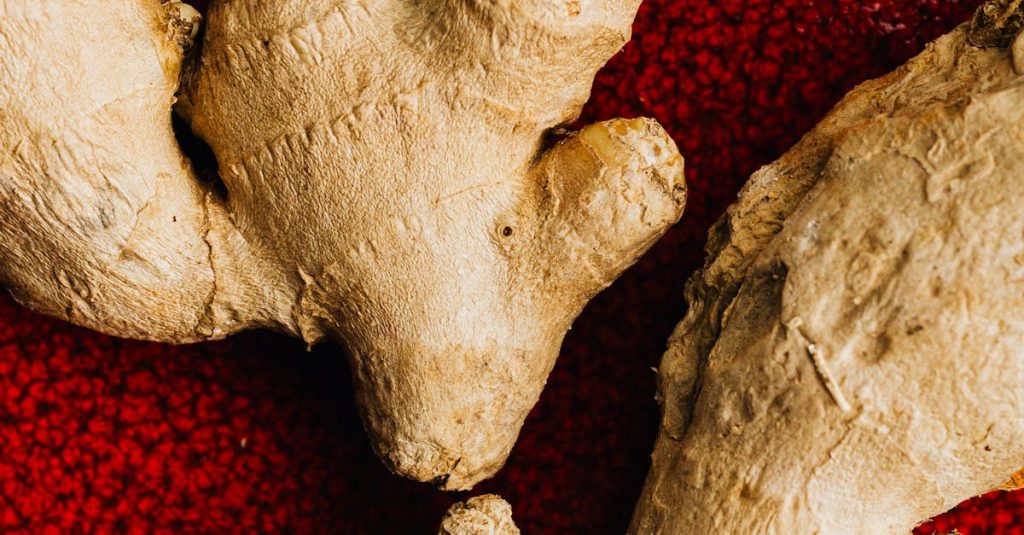 Macro shot of fresh ginger root on a textured red plate, highlighting its natural detail.