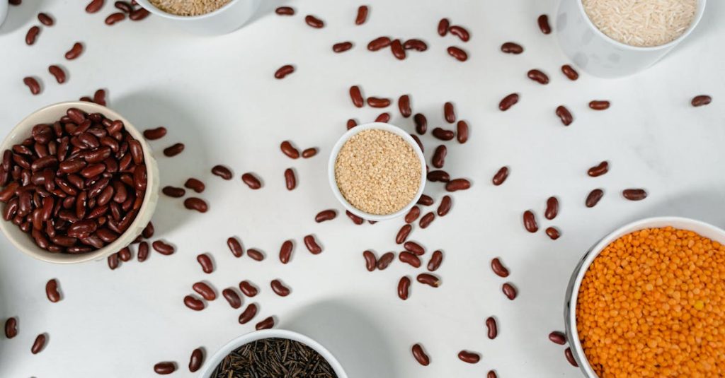 Top view of various grains and pulses in bowls on a white surface.