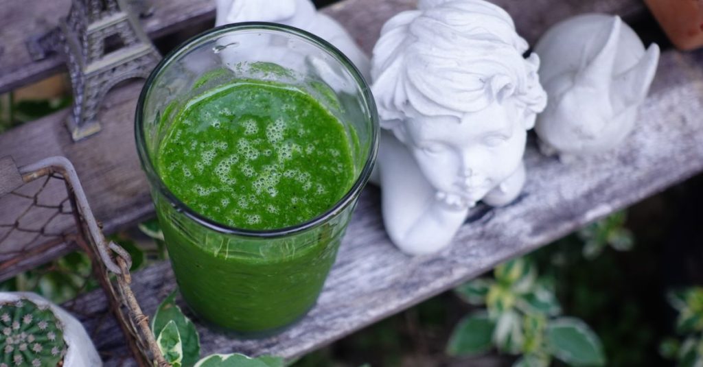 A vibrant green smoothie next to angel statue and Eiffel Tower model outdoors.