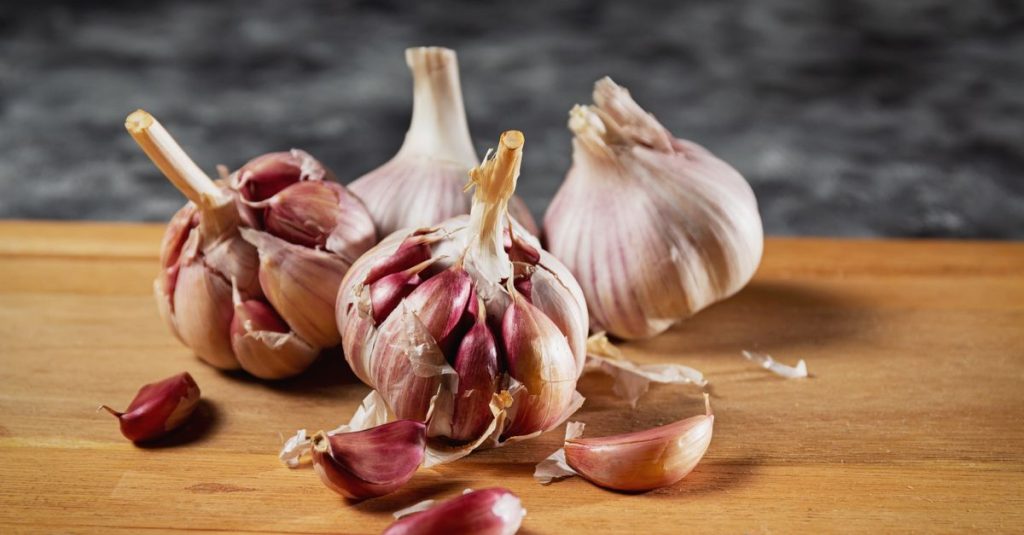 Close-up of fresh garlic bulbs and cloves on a wooden cutting board.