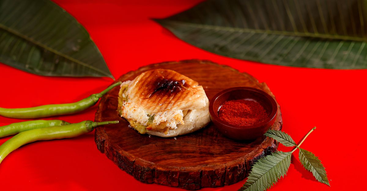 A grilled sandwich with spices on a wooden plate, set on a vibrant red background.