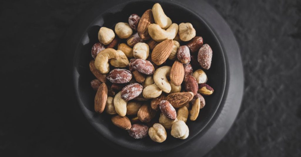 Top view of a variety of mixed nuts in a black bowl, showcasing almonds, cashews, and hazelnuts.