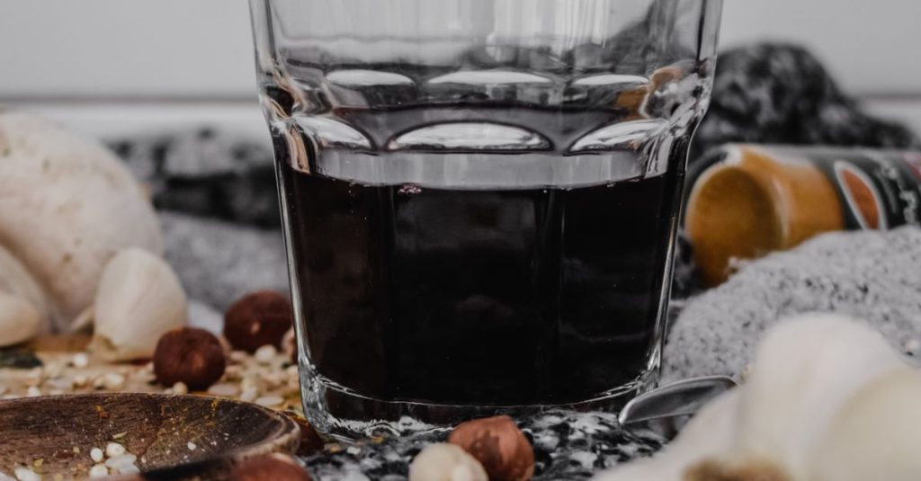 Glass of dark beverage surrounded by assorted nuts and garlic cloves.