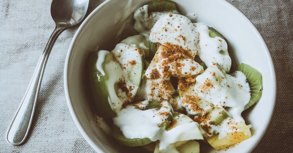 Fresh kiwi and pineapple slices topped with yogurt and cinnamon in a white bowl, perfect for a healthy breakfast.