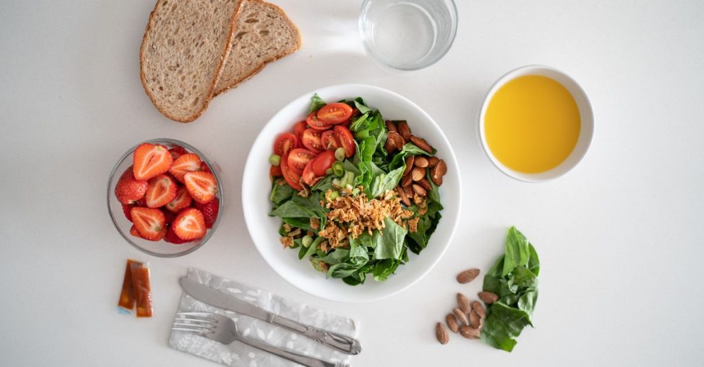 Top view of a healthy salad and fresh ingredients with bread and juice on a white surface.